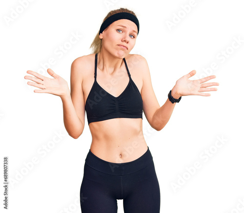 Young beautiful blonde woman wearing sportswear clueless and confused expression with arms and hands raised. doubt concept.