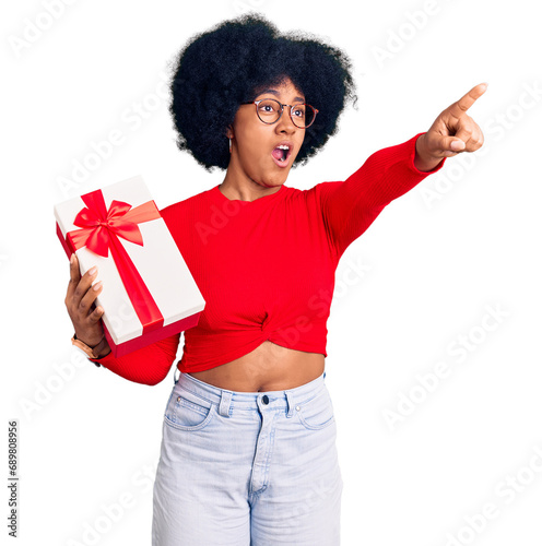 Young african american girl holding gift pointing with finger surprised ahead, open mouth amazed expression, something on the front