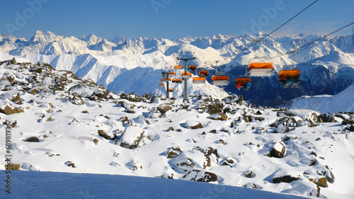 Orange chairlift with unrecognizable skiers in Samnaun - Ischgl - Paznaun ski resort, located in Austria and Switzerland. Winter, ski, chair lift. photo