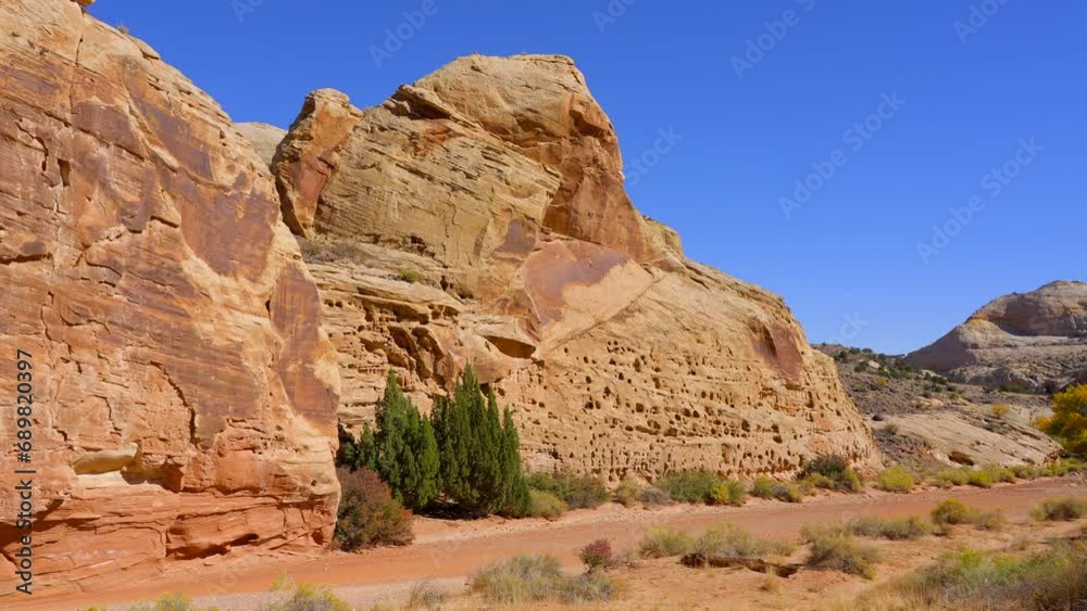 Establishing shot of mountain trail with red rocks background in Grand Wash Trail, Capital Reef National Park, Utah, North America. Day time on October 2023. Still camera view. ProRes 422 HQ. Establishing shot of mountain trail with red rocks background in Grand Wash Trail, Capital Reef National Park, Utah, North America. Day time on October 2023. Still camera view. ProRes 422 HQ.