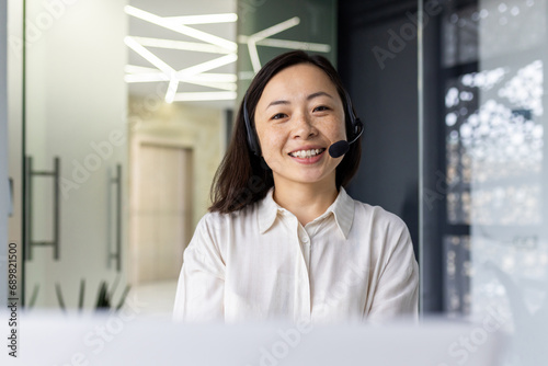 Portrait of online support worker, asian woman with headset phone smiling and looking at camera, businesswoman working in laptop at workplace inside office, call center call center support service.