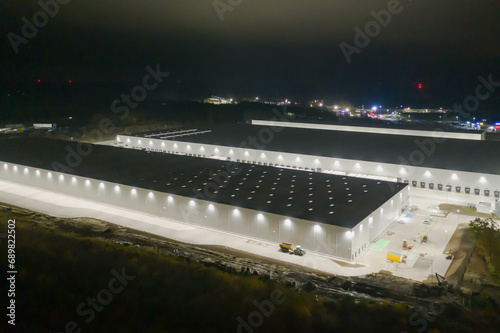 Centrum logistyczne w nocnych ciemnościach. Teren wokół jak i budynki oświetlone są sztucznym światłem elektrycznym. Zdjęcie zrobione przy użyciu drona. © boguslavus