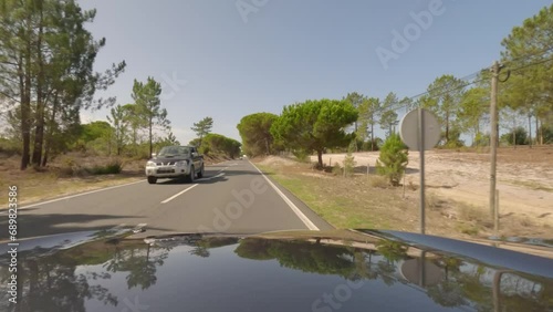 First person view, FPV, from dashcam of car driving along the Alentejo Coast in Portugal, passing cork oak trees and sand dunes. Road trip video in POV, with blue sky and clouds photo