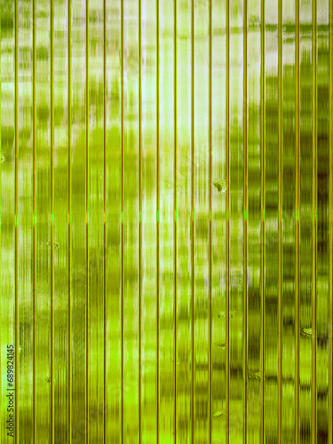 Texture of green embossed organic glass. Straight strips of glass are parallel and translucent. Drops of water are visible from above.
