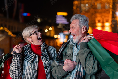 Excited senior couple looking at each other doing Christmas shopping walking with shopping bags. Two elderly people in good spirit after buying presents.