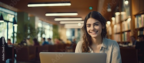 Education university and happy woman in library with laptop research and books for school project or exam Smile internet and college phd student studying with technology and elearning on campus photo