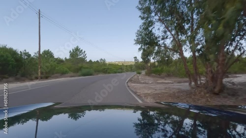 First person view, FPV, from dashcam of car driving along the Alentejo Coast in Portugal, passing cork oak trees and sand dunes. Road trip video in POV, with blue and clear sky on an empty road photo