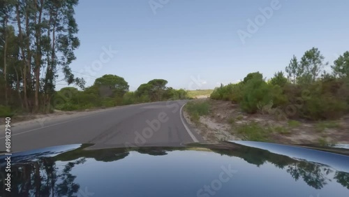 First person view, FPV, from dashcam of car driving along the Alentejo Coast in Portugal, passing cork oak trees and sand dunes. Road trip video in POV, with blue and clear sky on an empty road photo