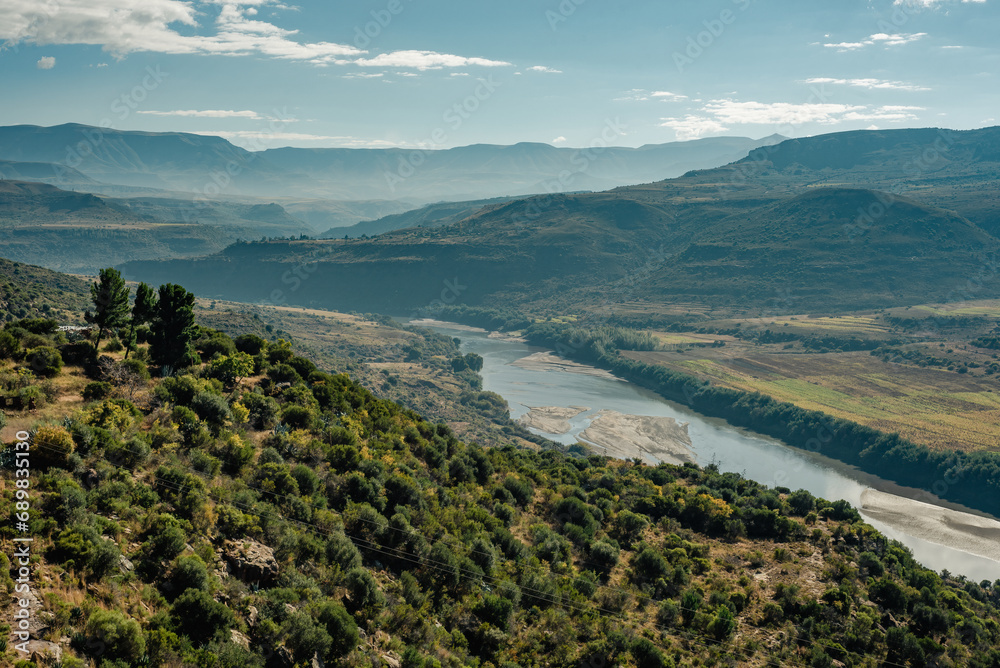 A river runs through green hills on a sunny, hazy day in Lesotho