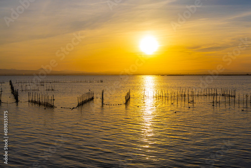 A lake with fish nets and sunny path against the backdrop of an orange sunset