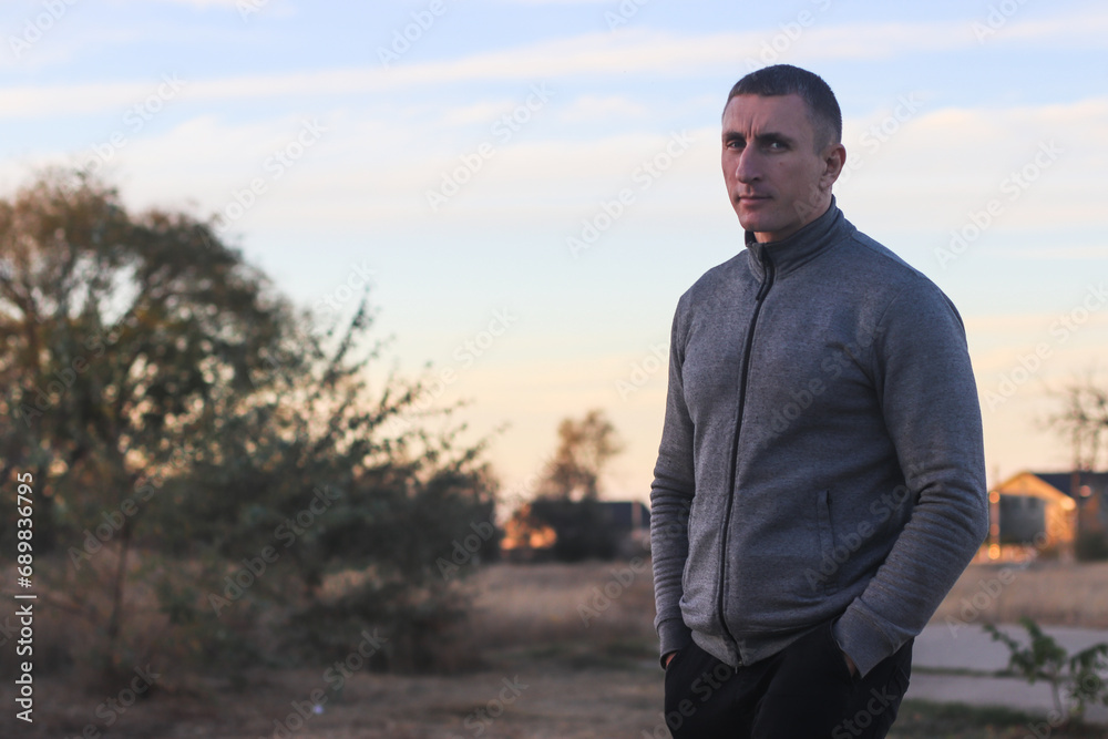 adult man in a gray sweater on an evening walk outside the city adult man in a gray sweater on an evening walk outside the city