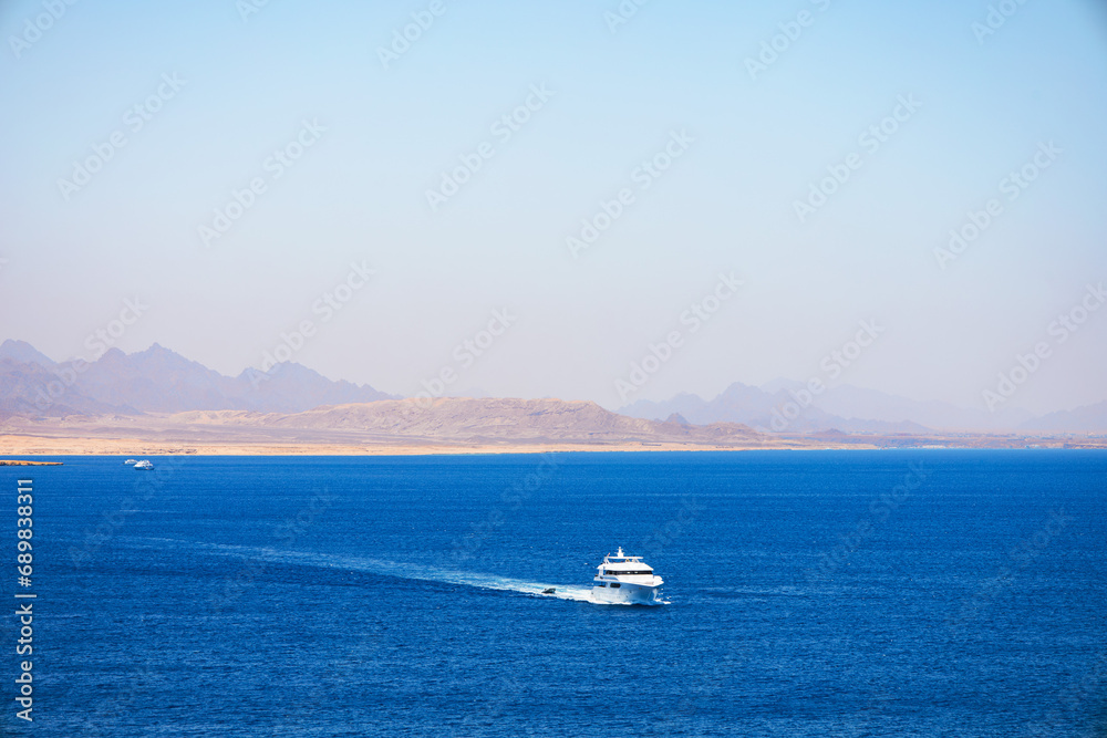 White boats on blue color of Red Sea with sandy and rocky coast in the background. Popular place of tourists. Ras Muhammad in Egypt at the southern extreme of the Sinai Peninsula. Travel concept