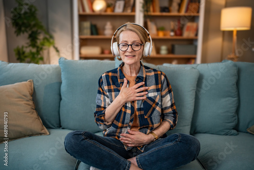 A mature woman listens to a guided meditation on headphones, she is on the couch in her apartment and relaxes photo