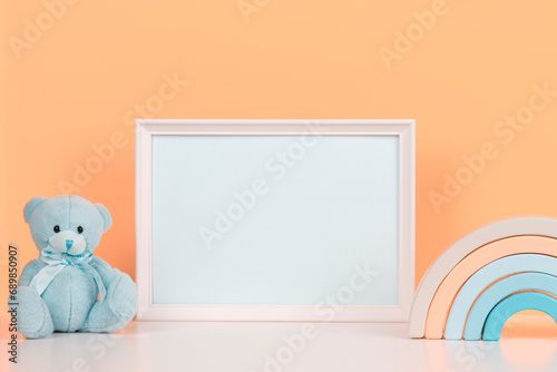 White blank horizontal wooden frame mockup, baby room art, empty wood blank frame with baby kid toys on white desk and peach pink background. Front view. Early education, kindergarten background