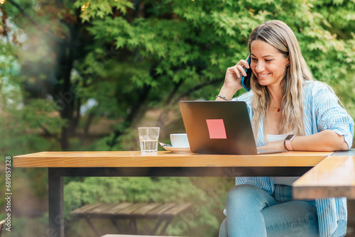 Seated in the café's garden, a businesswoman efficiently coordinates her call and online work, ensuring the seamless exchange of information with her business counterpart.