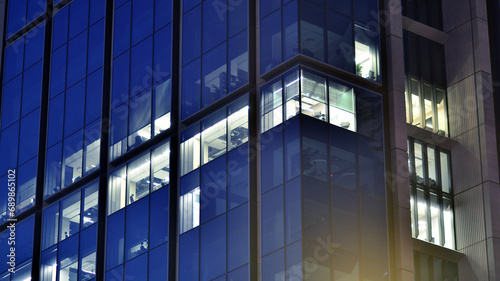 Fragment of the glass facade of a modern corporate building at night. Modern glass office in city. Big glowing windows in modern office buildings at night, in rows of windows light shines. 