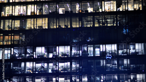 Fragment of the glass facade of a modern corporate building at night. Modern glass office in city. Big glowing windows in modern office buildings at night, in rows of windows light shines. 