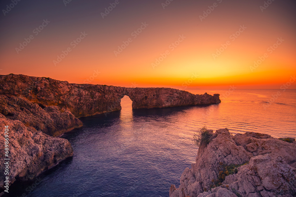 Krajobraz morski, pomarańczowy zachód słońca, skaliste wybrzeże wyspy Minorka (Menorca), Hiszpania	