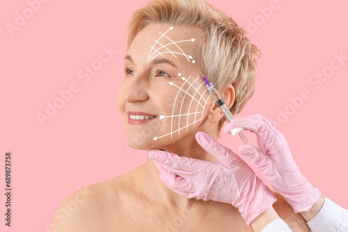 Mature woman receiving filler injection in face against pink background. Skin care concept photo