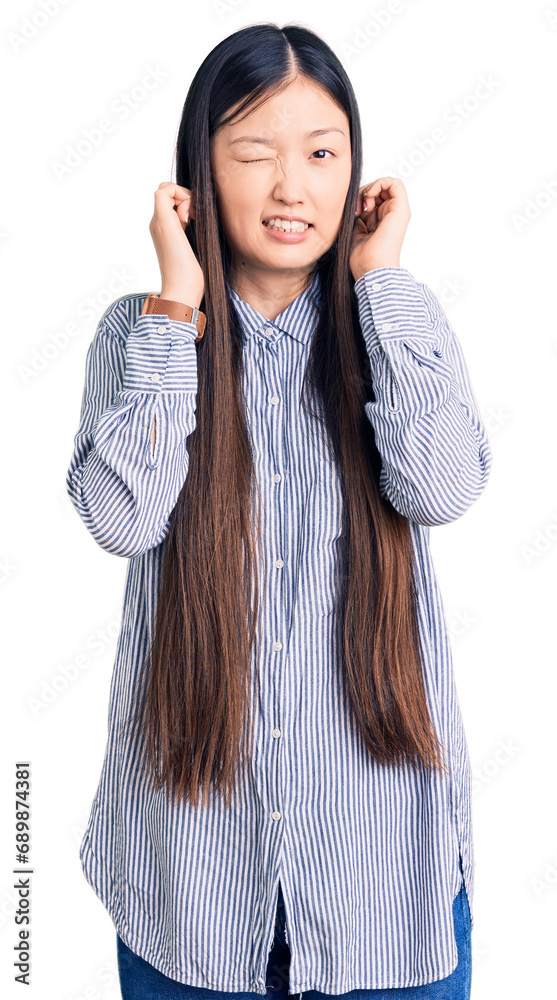 Young beautiful chinese woman wearing casual shirt covering ears with fingers with annoyed expression for the noise of loud music. deaf concept. Young beautiful chinese woman wearing casual shirt covering ears with fingers with annoyed expression for the noise of loud music. deaf concept.
