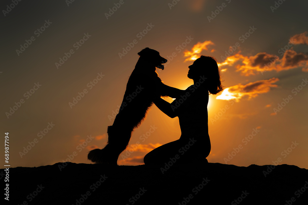 A dog hugs his owner at sunset. Dog and women silhouette