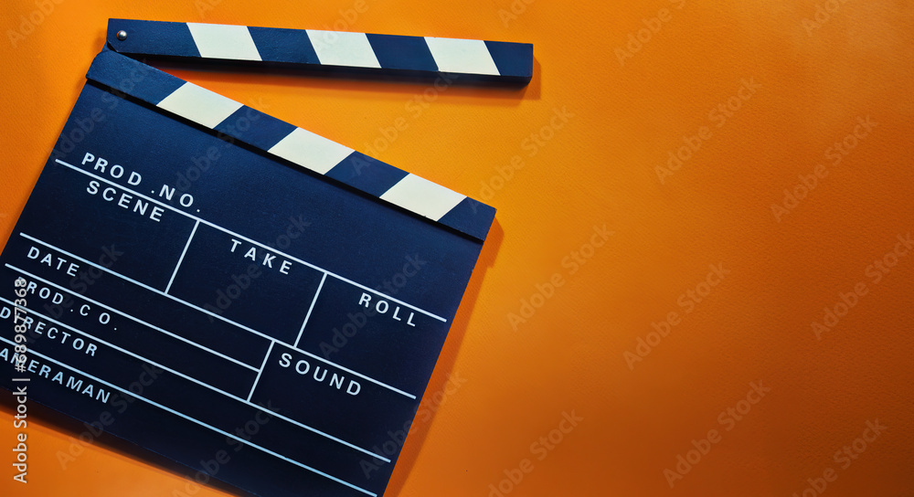 A clapperboard with an orange background. Symbol of filmmaking and video production. Professional type of equipment, used on films to assist in synchronizing of picture and sound