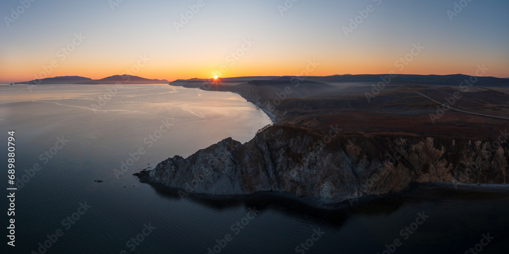 Beautiful sunset seascape. Aerial view of rocky cape and sea bay. Sun over the coast. Wide panorama. Popular natural tourist attraction. Cape Nyuklya, Sea of Okhotsk, Magadan region, Russian Far East.