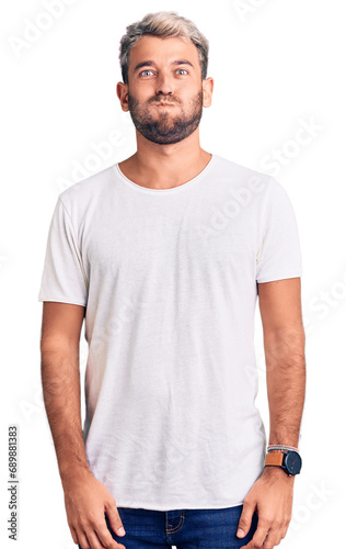 Young handsome blond man wearing casual t-shirt sticking tongue out happy with funny expression. emotion concept.
