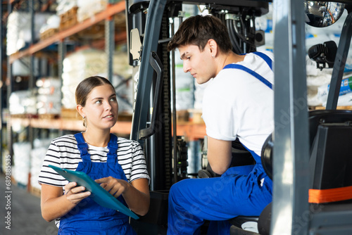 Young woman and young guy working on loader in warehouse check documents