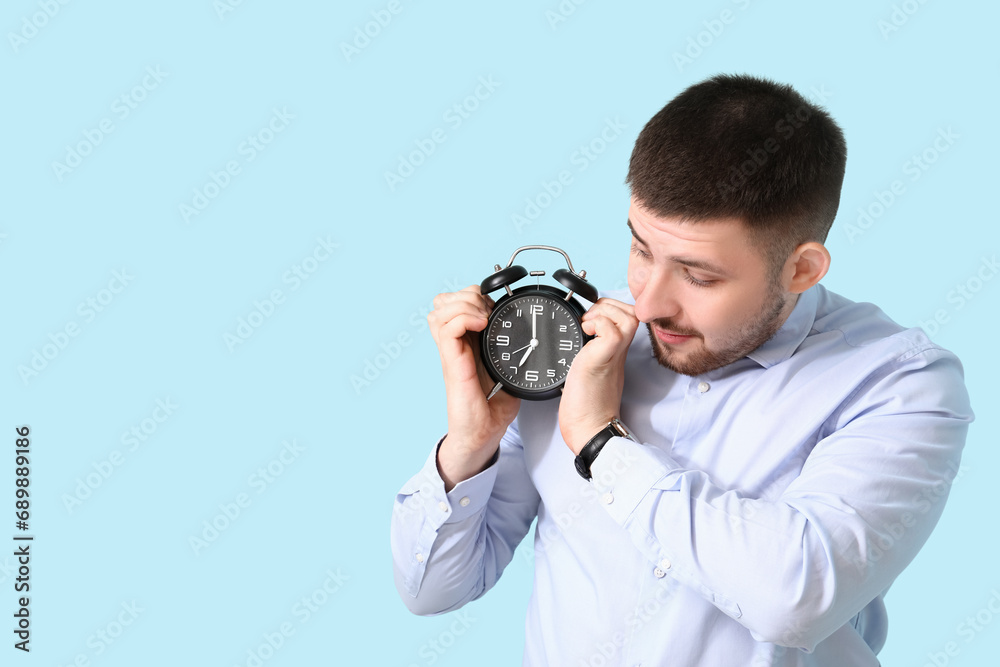 Young businessman with alarm clock on blue background. Time management concept Young businessman with alarm clock on blue background. Time management concept