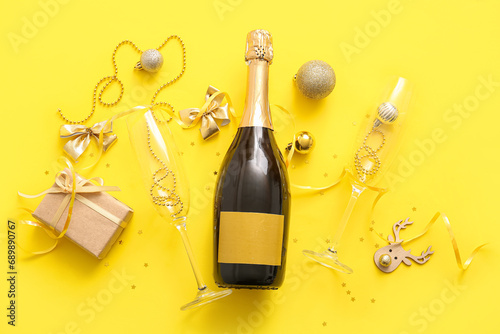 Bottle of champagne with glasses, Christmas decorations and gift box on yellow background