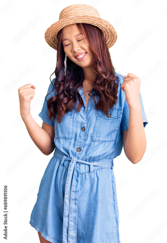 Young beautiful chinese girl wearing summer hat very happy and excited doing winner gesture with arms raised, smiling and screaming for success. celebration concept. Young beautiful chinese girl wearing summer hat very happy and excited doing winner gesture with arms raised, smiling and screaming for success. celebration concept.
