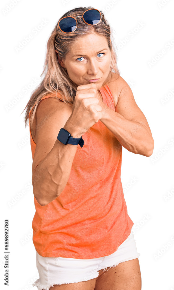 Middle age fit blonde woman wearing casual summer clothes and sunglasses ready to fight with fist defense gesture, angry and upset face, afraid of problem Middle age fit blonde woman wearing casual summer clothes and sunglasses ready to fight with fist defense gesture, angry and upset face, afraid of problem