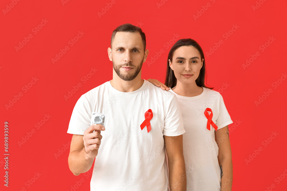 Young couple with red ribbons and condom on color background. AID awareness concept Young couple with red ribbons and condom on color background. AID awareness concept