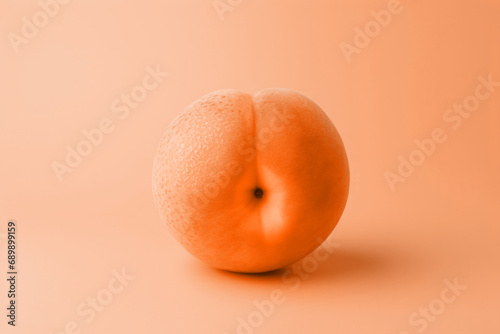 A single ripe peach fruit on minimal peach fuzz color background. Modern trendy tone hue shade