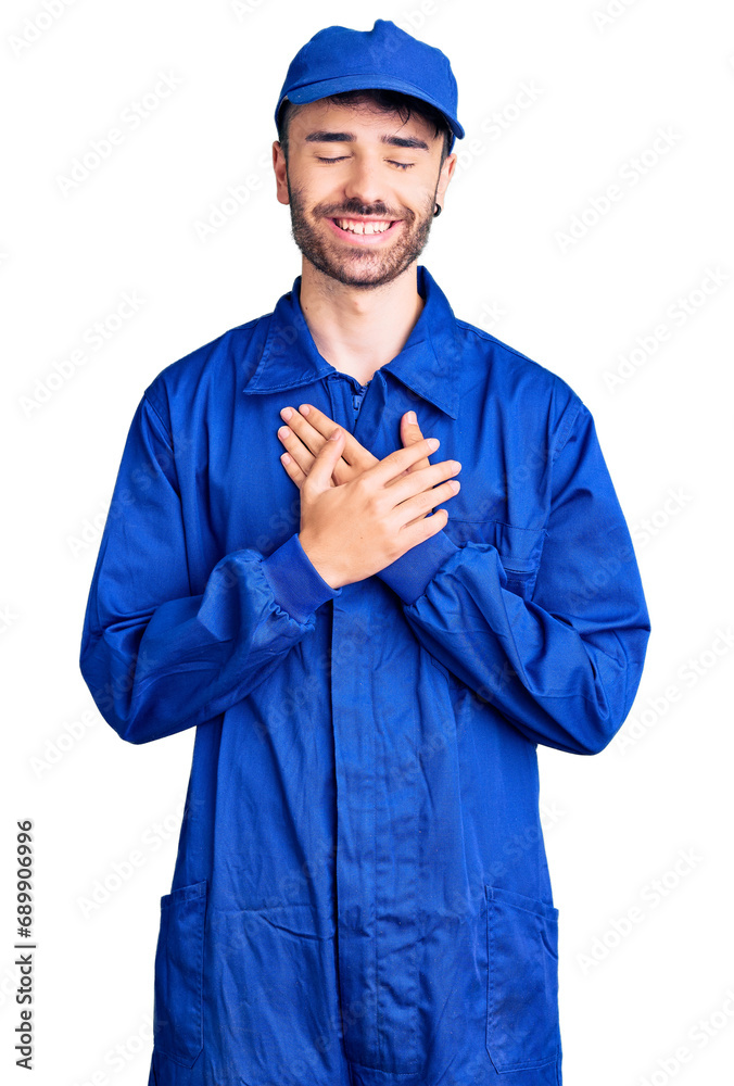 Young hispanic man wearing painter uniform smiling with hands on chest with closed eyes and grateful gesture on face. health concept. Young hispanic man wearing painter uniform smiling with hands on chest with closed eyes and grateful gesture on face. health concept.