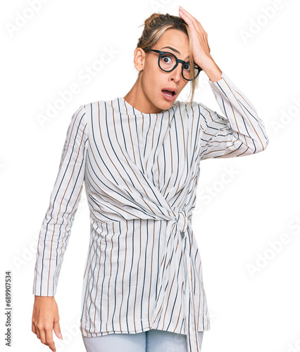 Beautiful blonde woman wearing business shirt and glasses surprised with hand on head for mistake, remember error. forgot, bad memory concept.