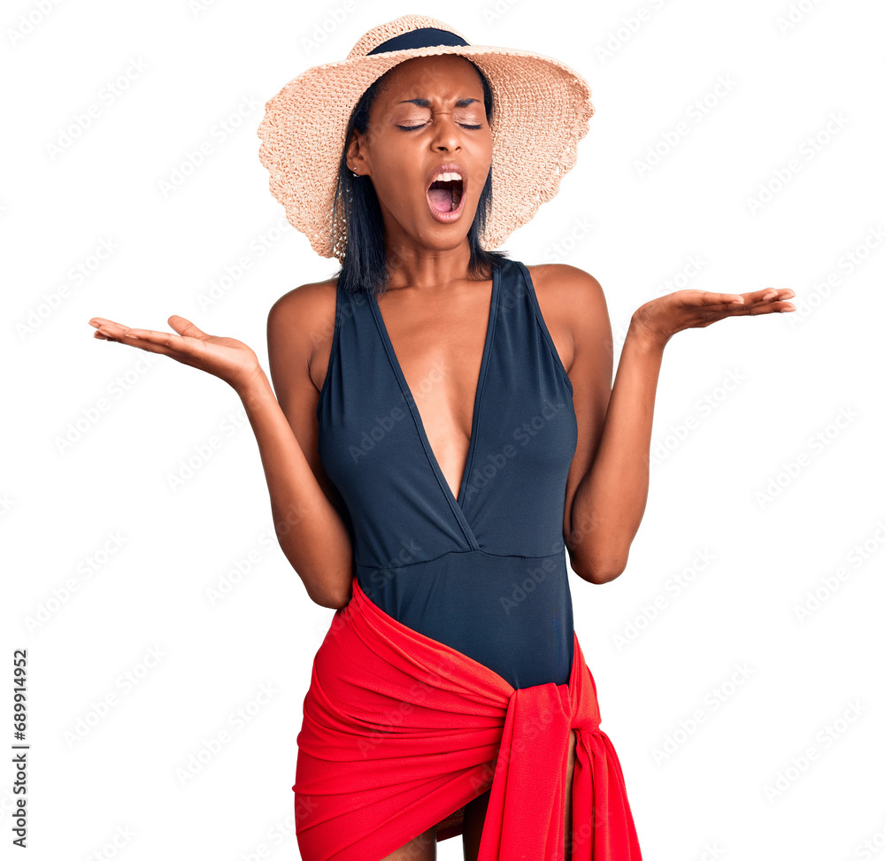 Young african american woman wearing swimsuit and summer hat celebrating mad and crazy for success with arms raised and closed eyes screaming excited. winner concept Young african american woman wearing swimsuit and summer hat celebrating mad and crazy for success with arms raised and closed eyes screaming excited. winner concept