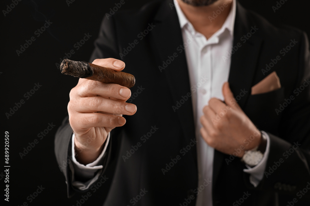 Man in elegant suit smoking cigar on black background, closeup