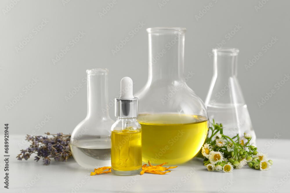 Cosmetic oil, laboratory dishware and flowers on white table