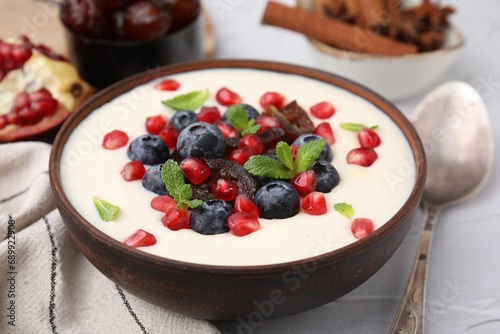 Delicious semolina pudding with blueberries, pomegranate, dates and mint in bowl on white table, closeup