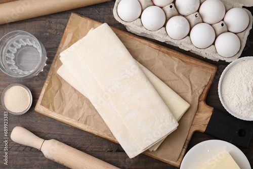 Raw puff pastry dough and ingredients on wooden table, flat lay photo