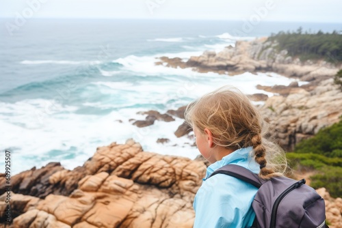 A young girl with a backpack stands on top of a mountain and admires the panorama