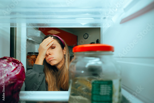 Woman Looking in the Fridge Having Nothing to Eat. Hungry millennial girl searching for a snack in her empty refrigerator 
