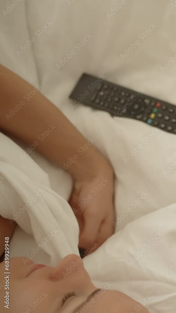 Vertical video. Top View of a Young Woman in a White Bed in the Morning Using a Remote Control to Turn On the Television. Vertical video. Top View of a Young Woman in a White Bed in the Morning Using a Remote Control to Turn On the Television.