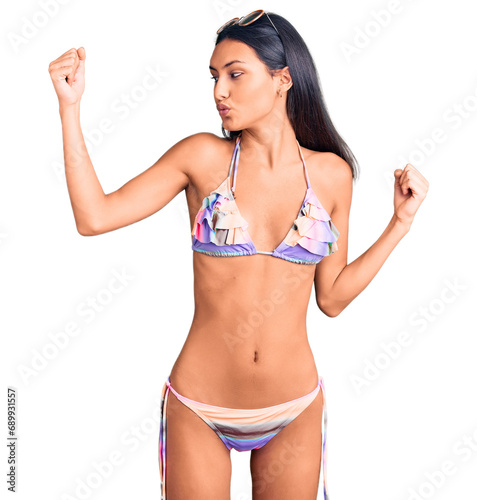 Young beautiful latin girl wearing bikini and sunglasses showing arms muscles smiling proud. fitness concept.