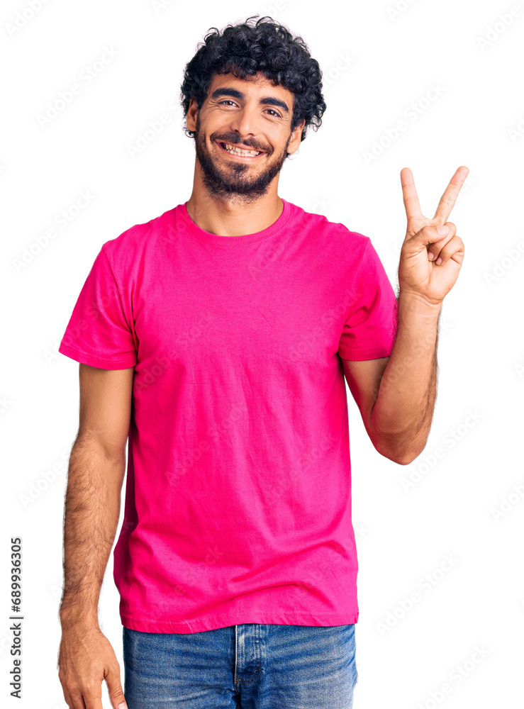 Handsome young man with curly hair and bear wearing casual pink tshirt showing and pointing up with fingers number two while smiling confident and happy. Handsome young man with curly hair and bear wearing casual pink tshirt showing and pointing up with fingers number two while smiling confident and happy.