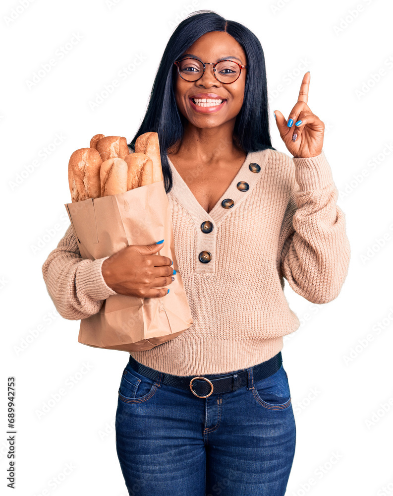 Young african american woman holding paper bag with bread surprised with an idea or question pointing finger with happy face, number one
