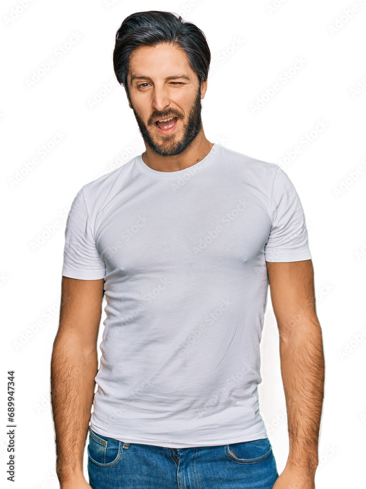 Young hispanic man wearing casual white t shirt winking looking at the camera with sexy expression, cheerful and happy face. Young hispanic man wearing casual white t shirt winking looking at the camera with sexy expression, cheerful and happy face.