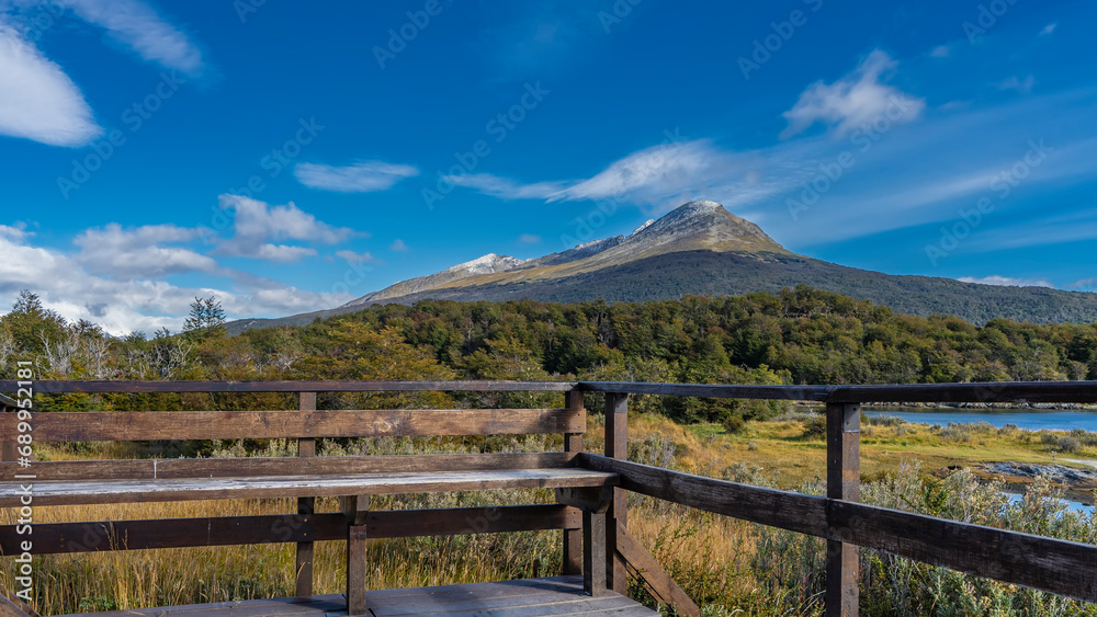 The landscape of Patagonia is visible from the observation deck. A blue lake, a meadow, thickets of green forest in the valley. A picturesque mountain against a azure sky and clouds. Argentina.